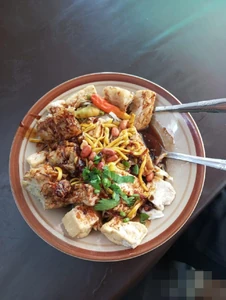 This dish is called "Tahu Ketupat." It's spicy and can be enjoyed for a reasonable price. The dish contains fried tofu, mixed veggie, and seafood tempura, steamed rice, noodles, cabbage, and peanut sauce.